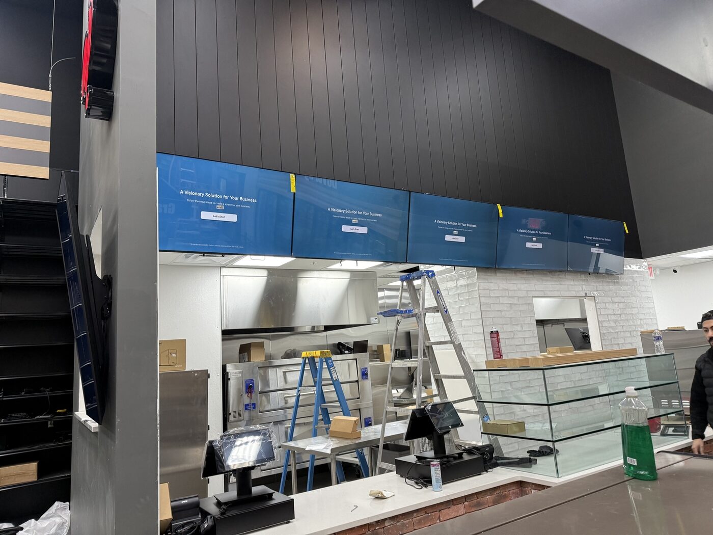 Row of five public-view monitors installed in a market and deli