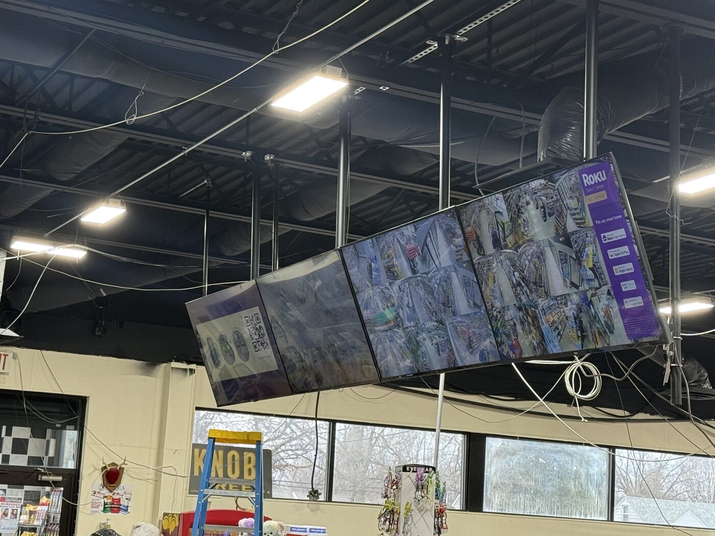 Four suspended monitors showing security feeds in a retail store